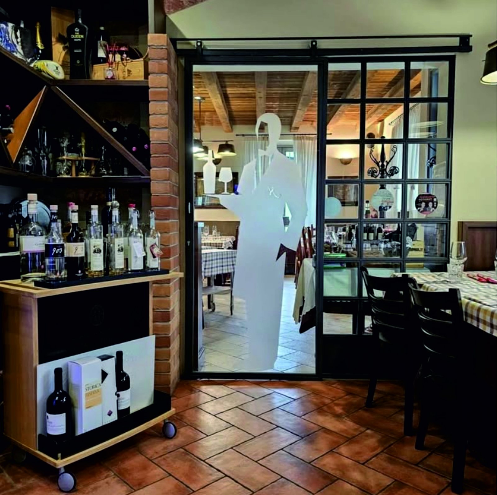 Sala interna della trattoria con tavoli apparecchiati e carrello dei vini
